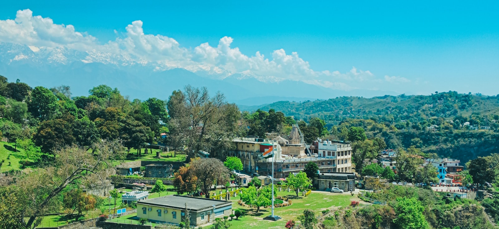 Buildings and trees in Kangra town below distant snow-covered mountains.