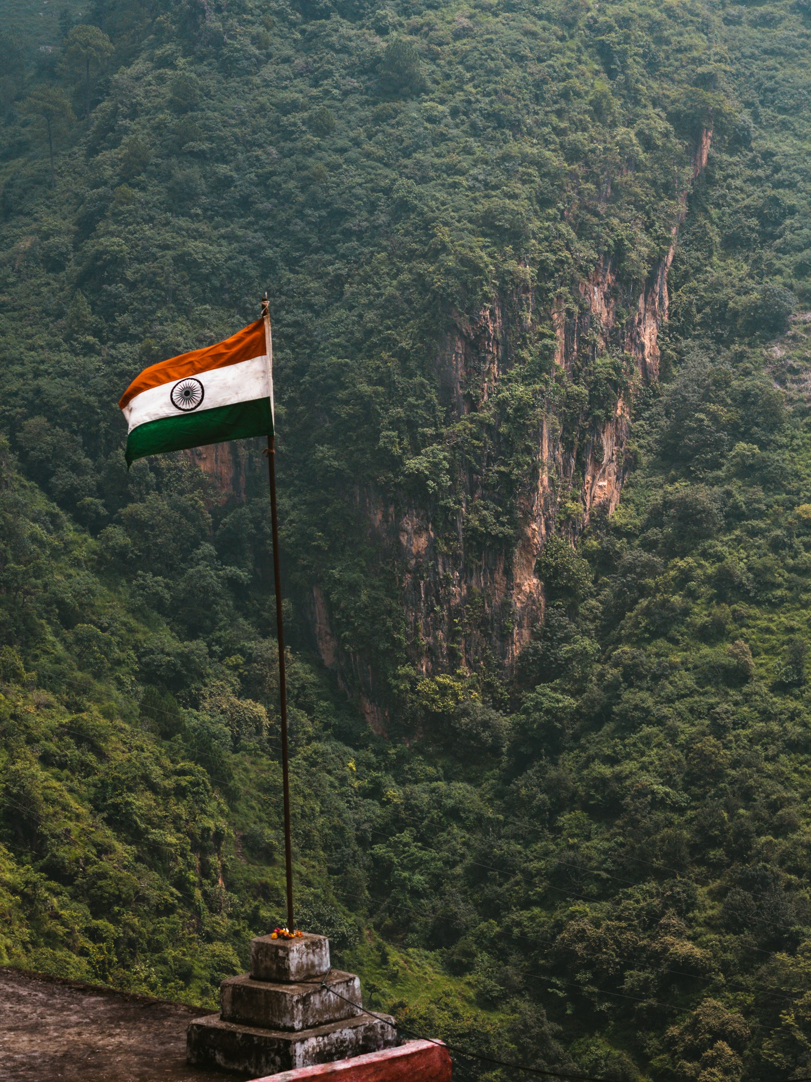 An Indian flag above a forested valley and rocky cliff in Sirmaur, Himachal Pradesh.