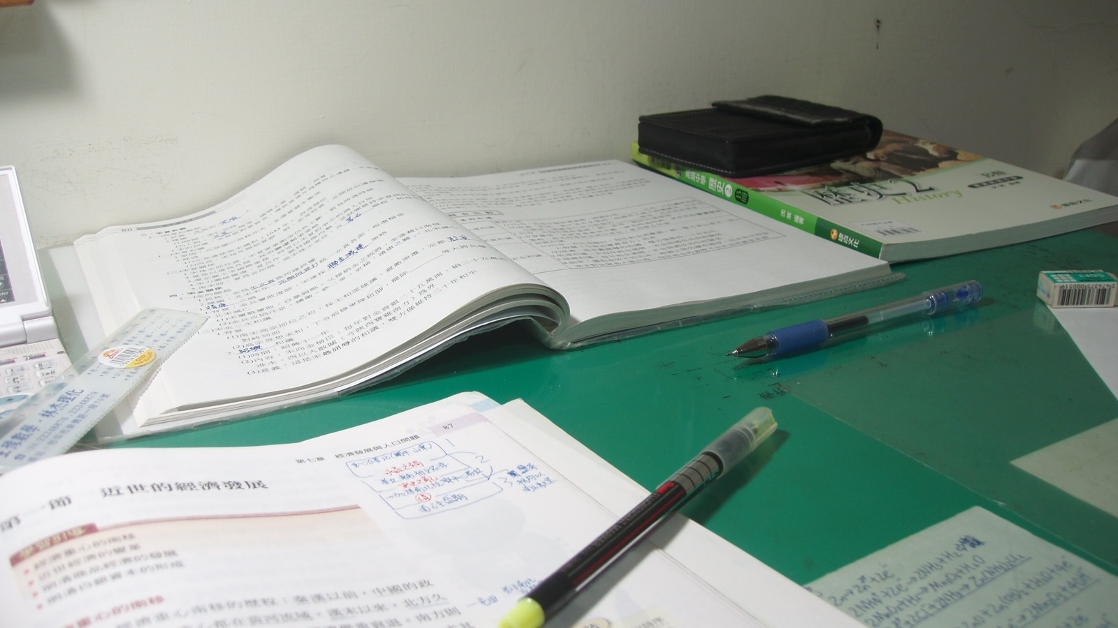 Open textbooks, handwritten study notes, pens and a pencil case arranged on a desk.